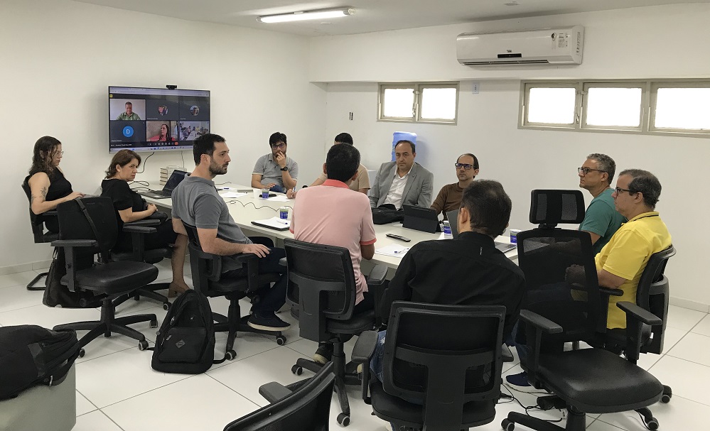 Representantes do NEES e do Odoo em reunião sentados ao redor de uma mesa retangular branca